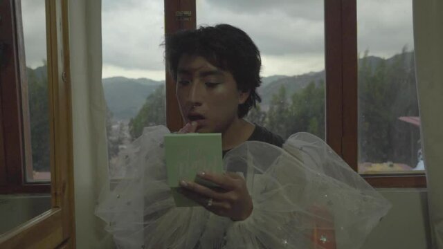 Joven queer maquillado pint&aacute;ndose los labios en su habitaci&oacute;n 