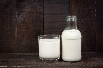 Milk in bottle and glass on rustic wooden background. 