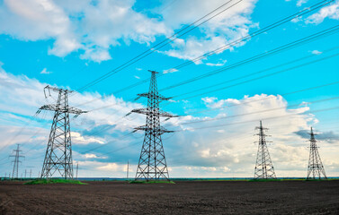 High voltage lines and power pylons in a flat and agricultural landscape on a sunny day with clouds...
