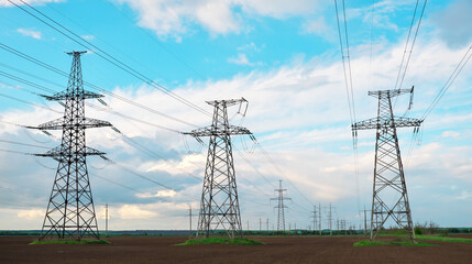 High voltage lines and power pylons in a flat and agricultural landscape on a sunny day with clouds in the blue sky.