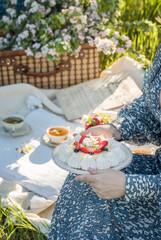 Cute picnic in the spring garden. The girl's hand holding a delicate dessert with meringue.