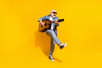 Poster Full length photo of cool happy positive old man dance hold guitar wear sunglass isolated on yellow color background © deagreez