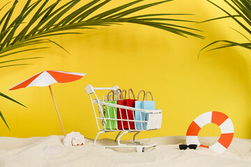 Summer shopping bags in cart on the beach with sand, paper accessories and palm leaves