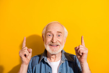 Photo of astonished cheerful man beaming smile direct fingers up empty space isolated on yellow...