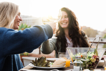 Happy people eating vegan food cheering with wine outdoors in summer sunset at patio restaurant -...