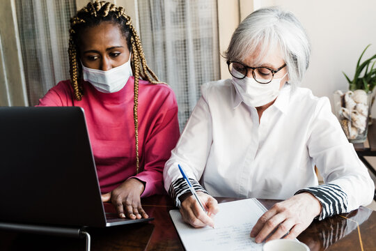 Multiracial young and senior business people with safety masks working inside modern office - Focus on senior woman face