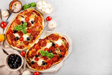 Two fresh and hot homemade italian pizzas with mozzarella, pepperoni sausages, olives and basil on the light gray background top view copy space for text