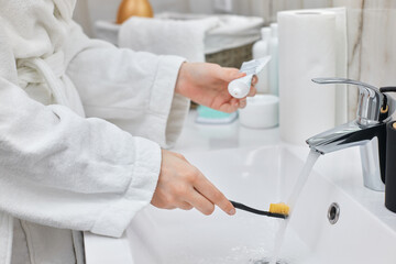 female hand holding toothbrush with paste in bathroom