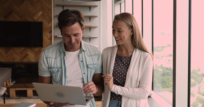 Millennial friendly businessman and businesswoman colleagues business partners browse internet search helpful information discuss online project working together standing in modern office with laptop