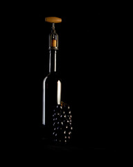 Red wine bottle with 2 glasses and bottle opener on black background.