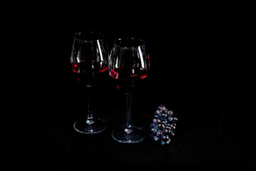 Red wine bottle with 2 glasses and bottle opener on black background.