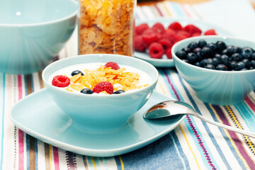 Breakfast of cornflakes and raspberries, blueberries and milk in a blue plate