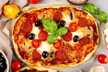 Fresh homemade italian pizza with mozzarella, pepperoni sausages, olives and basil close up top view