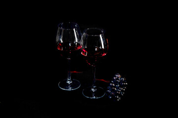 Red wine bottle with 2 glasses and bottle opener on black background.