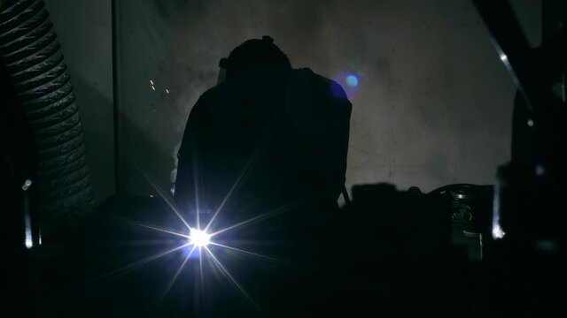 Back view welder man working using welding machine flashing bright sparks industrial equipment