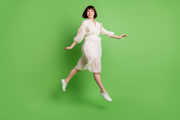 Full length body size photo woman wearing dotted dress jumping up running smiling isolated pastel green color background