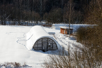 A greenhouse in an agricultural field is covered with snow