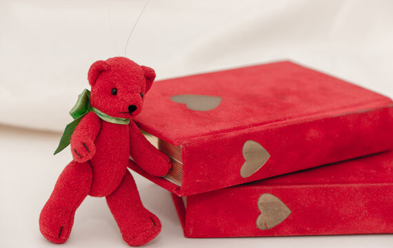 Small Red Ornament Teddy Bear With Green Bow-choker Poses Near Vintage Red Velvet Books With Golden Heart