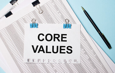 On a light blue background, documents, a pen and a sheet of paper on blue paper clips with the text CORE VALUES. Business concept.