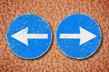 Old blue metallic arrow sign indicating to go left and right against an aged rusty metal wall -...