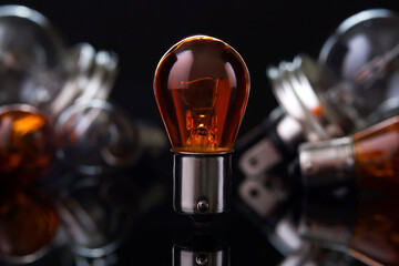 Orange car light bulb against blurred lamps on dark background, small depth of focus. Automotive...