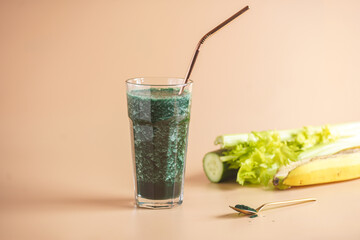 A glass of green healthy detox smoothie with vegetables and spirulina powder and a brass straw