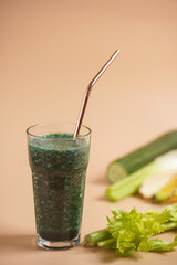 A glass of green healthy detox smoothie with vegetables and spirulina powder and a brass straw