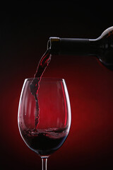 Fototapeta na wymiar Pouring red wine from bottle into glass on color background, closeup