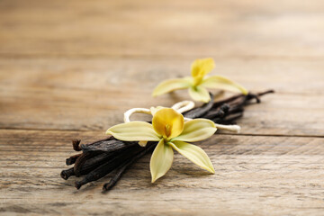 Beautiful vanilla flowers and sticks on wooden table, closeup