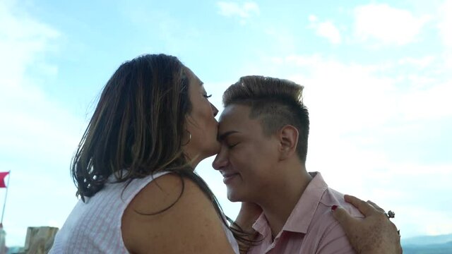 Madre besando la frente de su hijo gay con el cielo de fondo