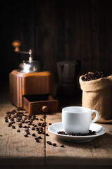 The white coffee cup on the dish. top the old wood table has coffee vintage grinder beans and Moka pot as dark tone background the Top copy space
