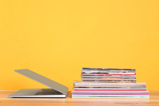 Laptop and stack of magazines on wooden table