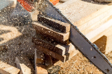 Close up of a woodcutter, sawing wooden boards chain saw in motion, sawdust fly to sides. Chainsaw in motion. Sawdust fly around.