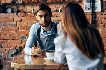 a man with a cup of coffee and all aprons at a cafe table and a woman in a shirt and red skirt cropped view