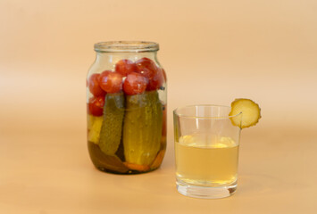 Fototapeta na wymiar Jar with canned cucumbers and tomatoes on a beige background. A glass of brine.