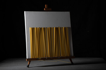 spaghetti in front of a frame that is on an easel. underneath a gray wooden board