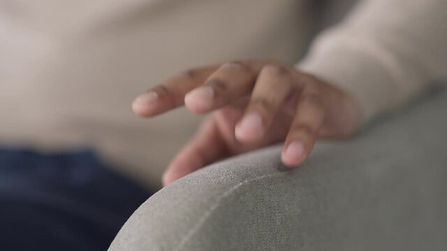 Close-up of male hand knocking fingers on couch. Unrecognizable impatient African American man waiting indoors