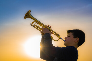 Teen boy playing trumpet against a beautiful sunset sky