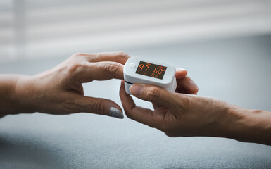 closeup daughter's hand putting oximeter on mom's finger for blood oxygen monitoring