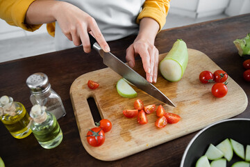 partial view of woman cutting zucchini near sliced cherry tomatoes on chopping board