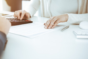 Accountant checking financial statement or counting by calculator income for tax form, hands closeup. Business woman sitting and working with colleague at the desk in office. Tax and Audit concept