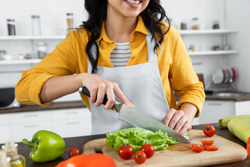cropped view of smiling woman cutting fresh lettuce near cherry tomatoes on wooden chopping board