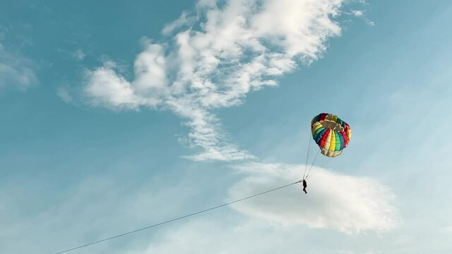 Wide far away slow motion shot of silhouetted parasailing skydiver with colourful parachute