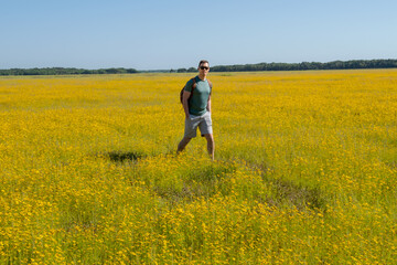 Handsome Healthy Young Man With Backpack Hiking Through Field of Yellow Wild Flowers