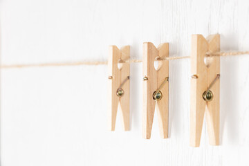 three wooden clothespins with a metal spring hang on a rope on a white background. selective focus