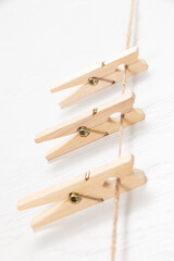 three wooden clothespins with a metal spring hang on a rope on a white background. selective focus