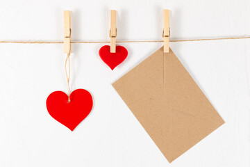 three wooden clothespins hang on a rope on a white background and hold a heart and an envelope. flat lay