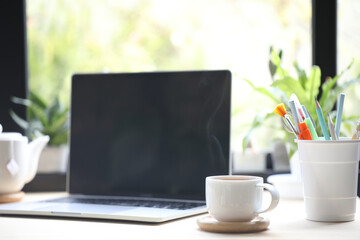 White coffee cup and laptop on table and plant pot in front of window