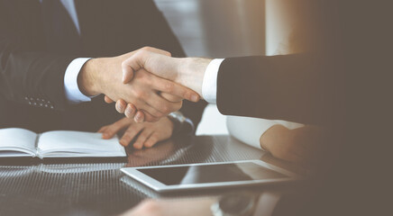 Unknown businessmen shaking hands above the glass desk in a modern office, close-up. Unknown business people at meeting. Teamwork, partnership and handshake concept