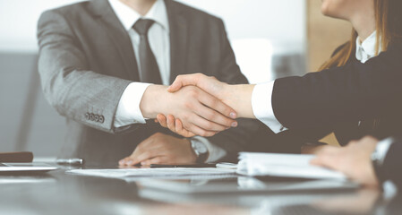 Unknown businessman shaking hands with his colleague or partner above the glass desk in modern office, close-up. Business people group at meeting